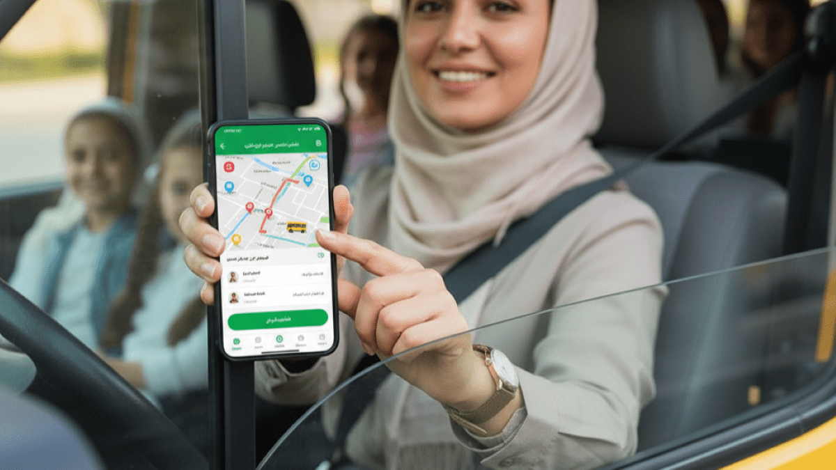 پیشنهاد: یک نمای بیرونی از یک ون سرویس مدرسه تمیز و مرتب در حال حرکت آرام در یک خیابان شهر (شلوغ نباشد). یا نمایی از داشبورد خودرو که راننده زن (دست‌هایش روی فرمان) با دقت به مسیر نگاه می‌کند و کنار او یک تبلت با نقشه مسیر دیده شود.